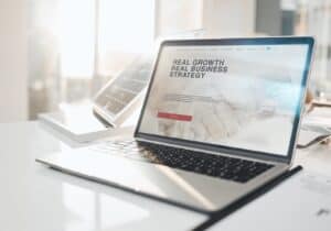 Hay una computadora portátil sobre un escritorio con un sitio web de bienes raíces.