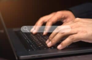 La mano de un hombre escribiendo en una computadora portátil con una barra de búsqueda.