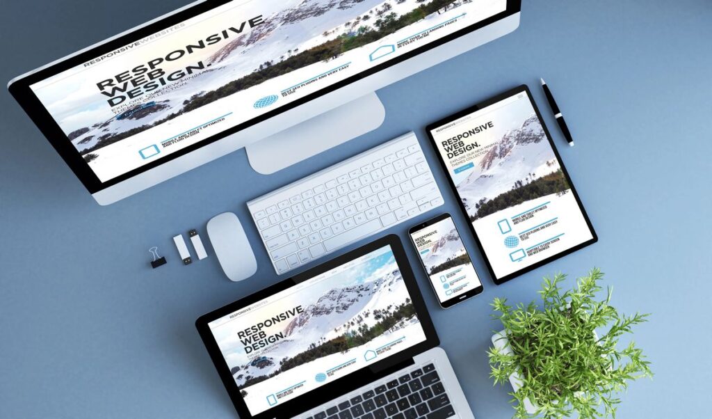 Vista aérea de varios dispositivos, incluyendo una computadora de escritorio, una computadora portátil, una tableta y un teléfono inteligente sobre un escritorio, mostrando páginas web en Tijuana con imágenes de montañas nevadas y el texto "Diseño Web Responsive".