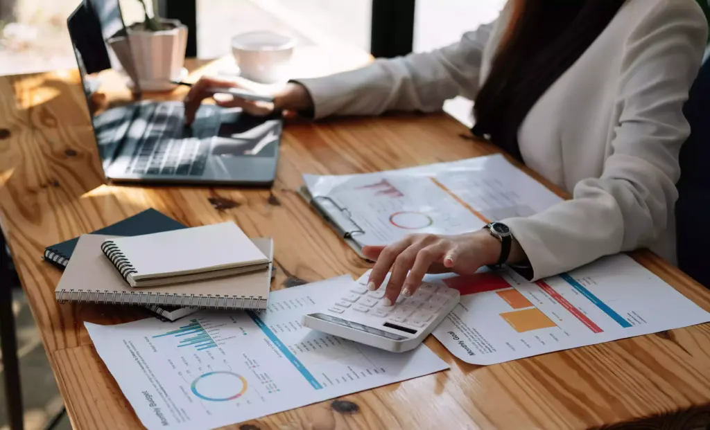 Inicio 8 Una persona vestida de negocios trabaja en un escritorio con una computadora portátil, calculadora, documentos con gráficos y un cuaderno, analizando datos de Google Trends para refinar su estrategia de contenido SEO.