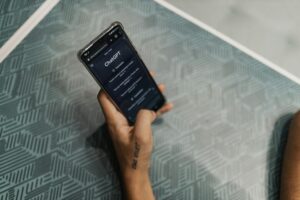 Una persona sostiene un smartphone con el sitio web ChatGPT abierto, sentada a una mesa con una superficie de motivos geométricos.