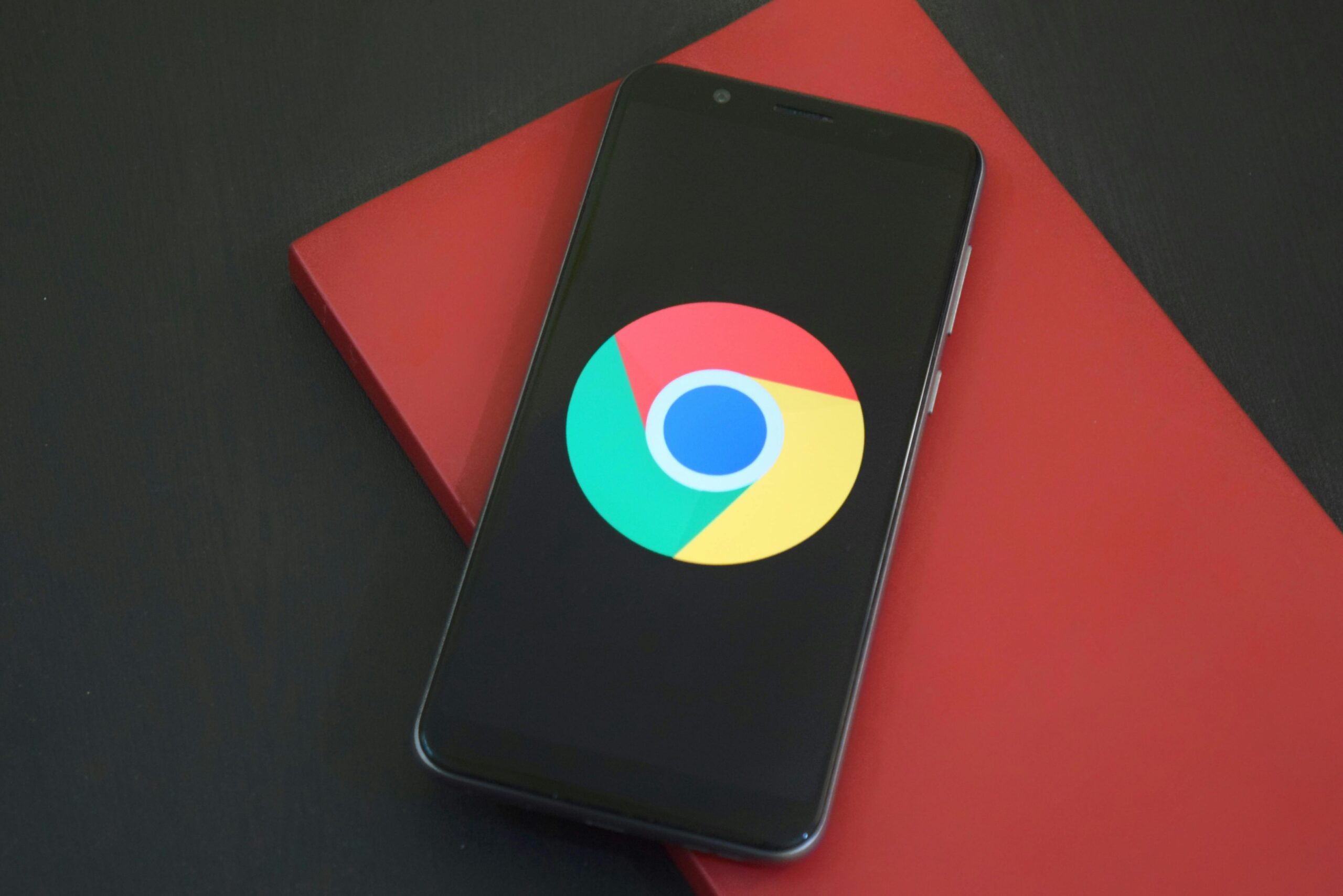 Un smartphone con el logotipo de Google Chrome descansa sobre un cuaderno rojo cerrado en una superficie oscura.