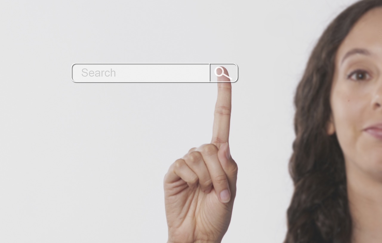 Una persona toca con el dedo índice una barra de búsqueda virtual, con el icono de búsqueda resaltado, sobre un fondo liso.
