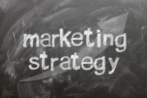 Las palabras "estrategia de marketing" están escritas con tiza blanca en una pizarra con una gran flecha apuntando a la derecha en el fondo.