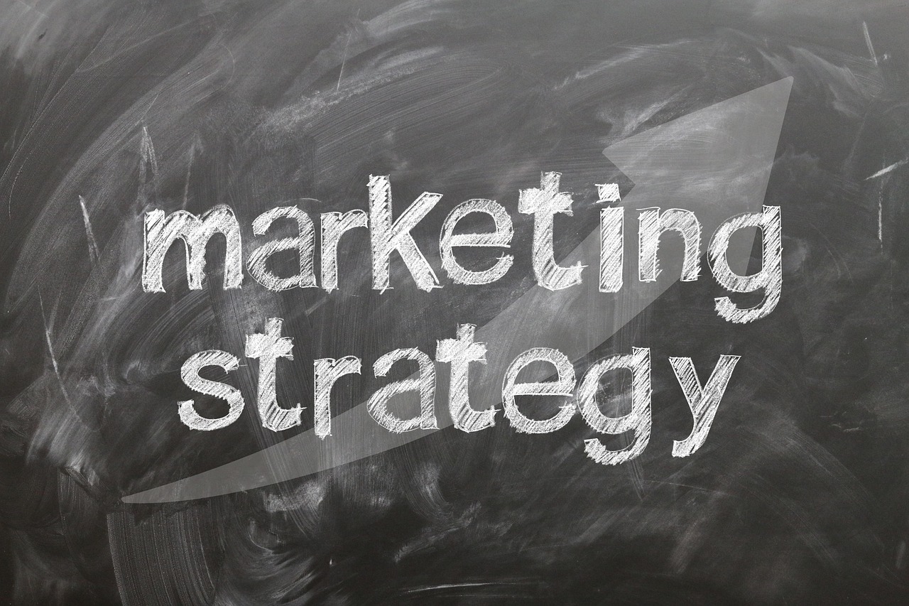 Las palabras "estrategia de marketing" están escritas con tiza blanca en una pizarra con una gran flecha apuntando a la derecha en el fondo.