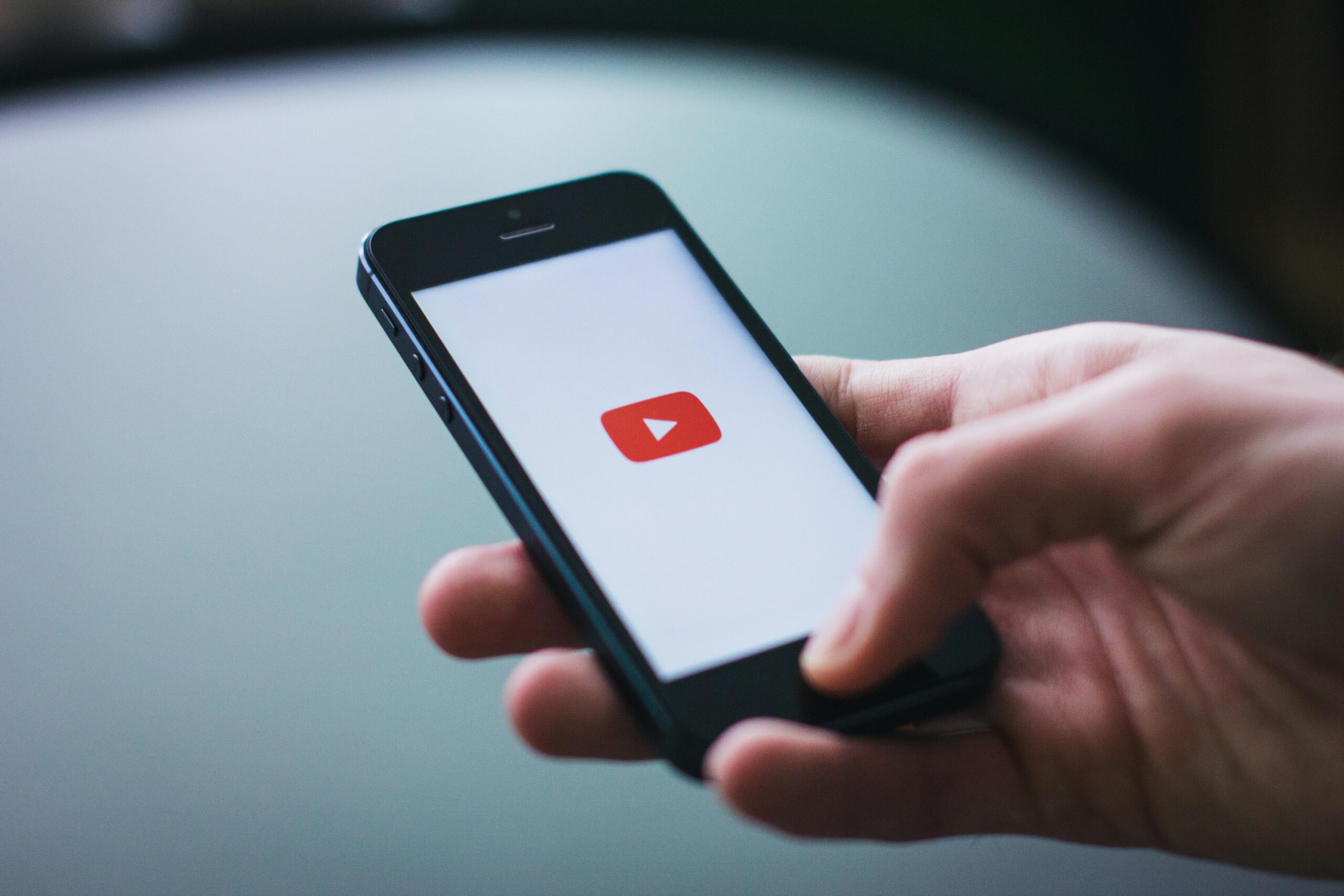 Persona con un smartphone en la mano mostrando la pantalla de carga de la aplicación YouTube con el logotipo de YouTube visible en la pantalla.