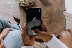Una persona sujeta un smartphone con la aplicación TikTok abierta, sentada en una mesa de madera con otra persona cerca.