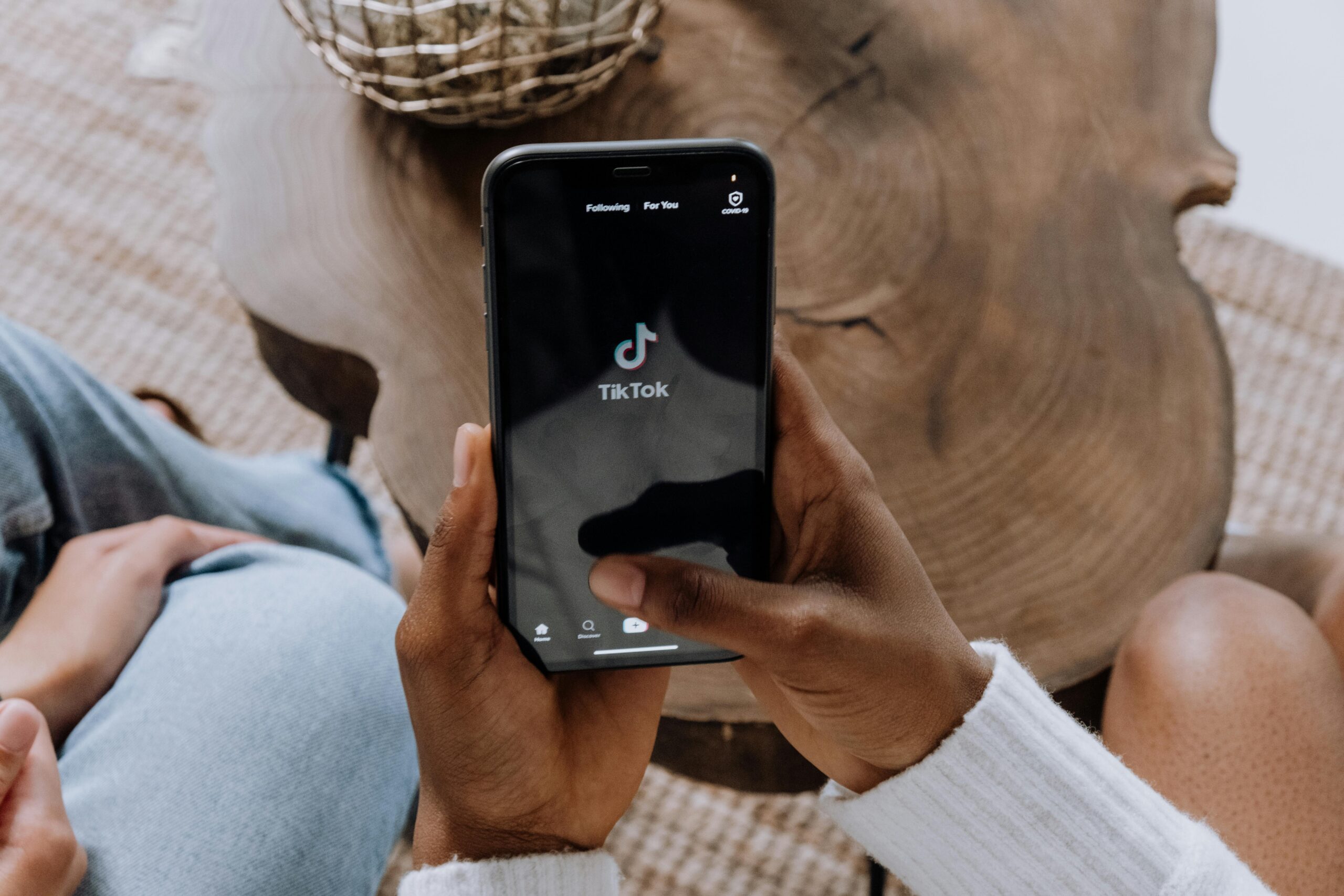 Una persona sujeta un smartphone con la aplicación TikTok abierta, sentada en una mesa de madera con otra persona cerca.