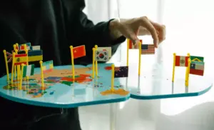 Una persona coloca banderas en miniatura de diferentes países en un mapa, ilustrando la SEO en diferentes países con banderas de Estados Unidos, China, Corea del Sur y otros.
