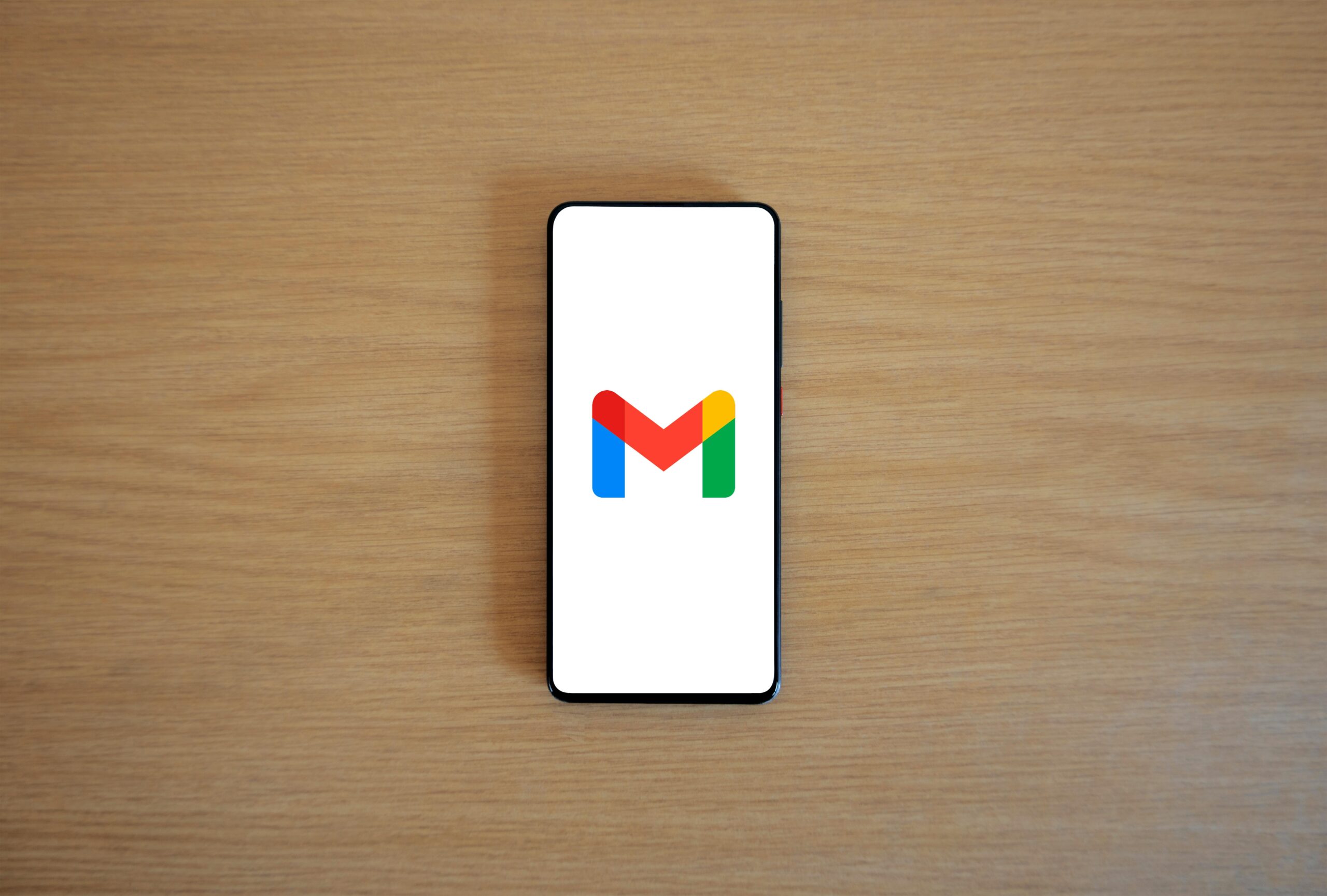 Un smartphone con el logotipo de Gmail en la pantalla descansa sobre una superficie de madera clara.