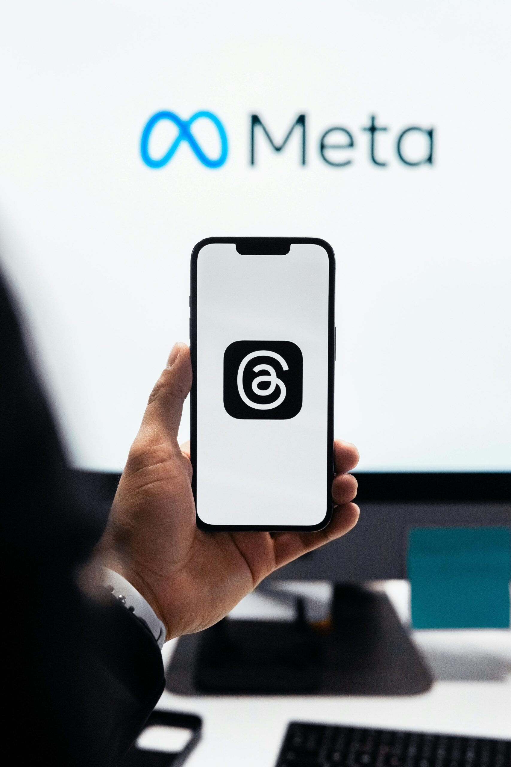 Una persona sostiene un smartphone con el logotipo de la aplicación Threads frente a la pantalla de un ordenador con el logotipo de Meta.