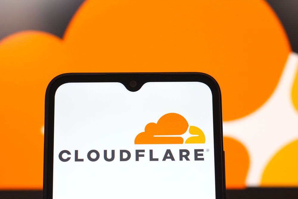 La pantalla de un smartphone muestra el logotipo de Cloudflare, con una versión ampliada del logotipo en naranja y blanco de fondo.
