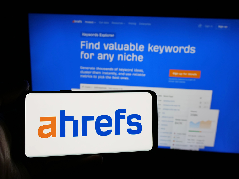 Un smartphone muestra el logotipo de Ahrefs delante de una pantalla de ordenador que muestra la página web del Explorador de Palabras Clave de Ahrefs.