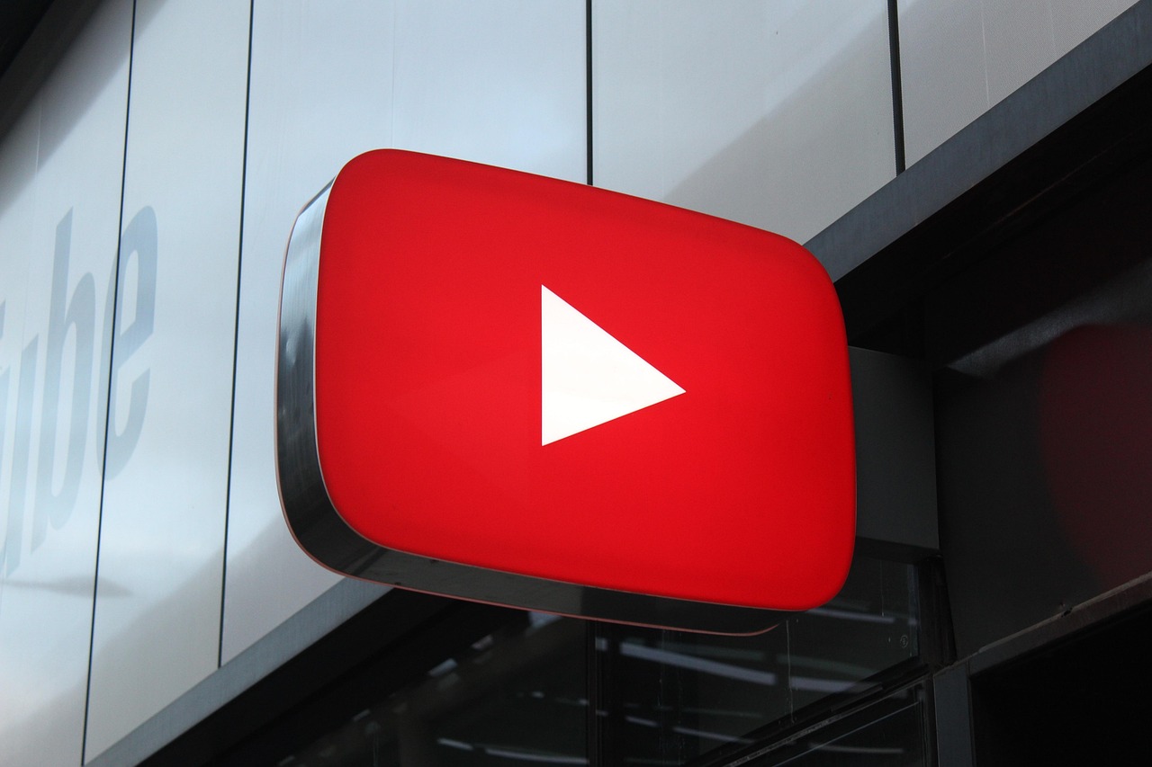 En el exterior de un edificio hay un gran cartel luminoso con el logotipo de YouTube y un botón de reproducción blanco sobre fondo rojo.