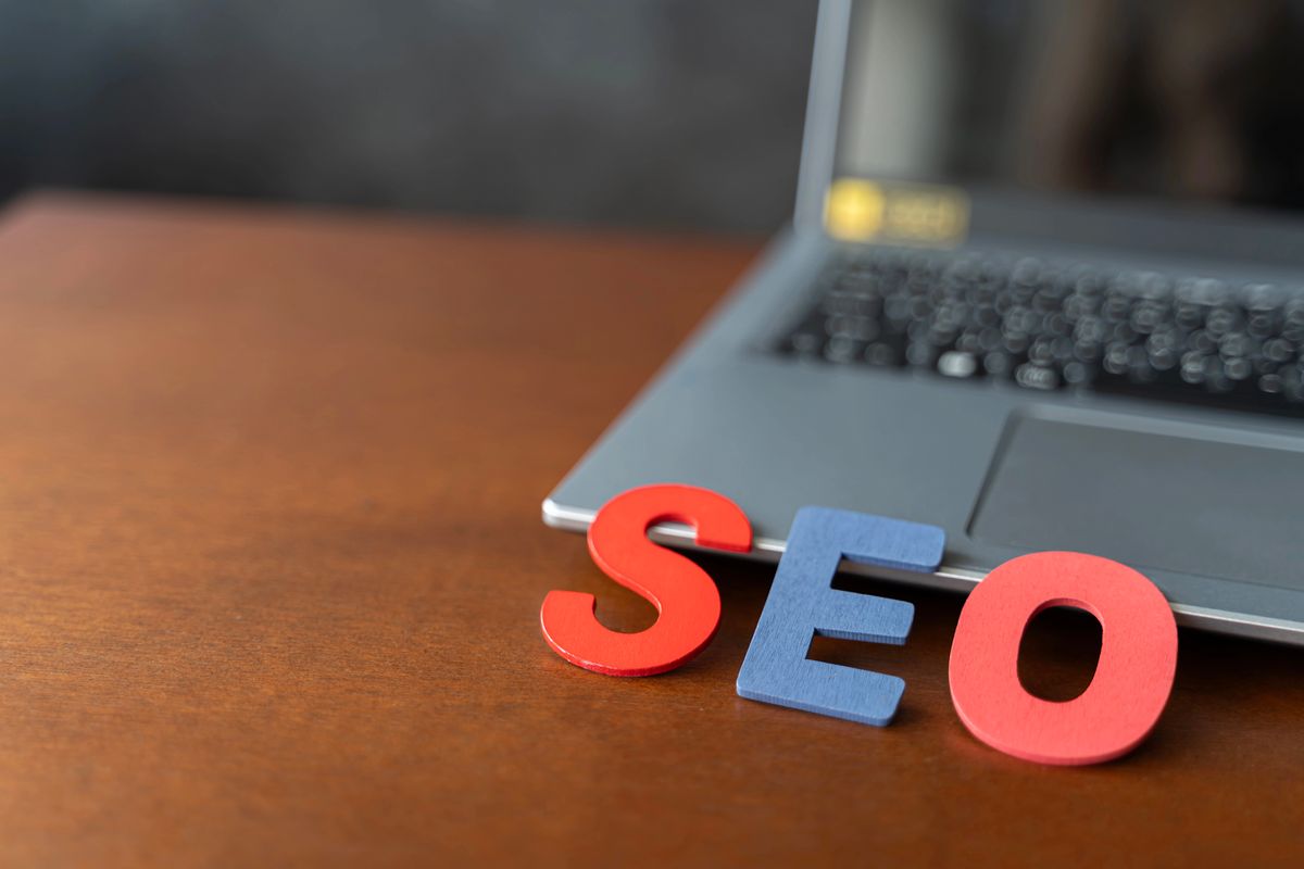 Letras de madera rojas y azules que deletrean "SEO" sobre una mesa de madera junto a un ordenador portátil abierto.