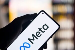Una mano sostiene un smartphone que muestra el logotipo y el nombre de Meta en su pantalla, con un fondo borroso de luces.