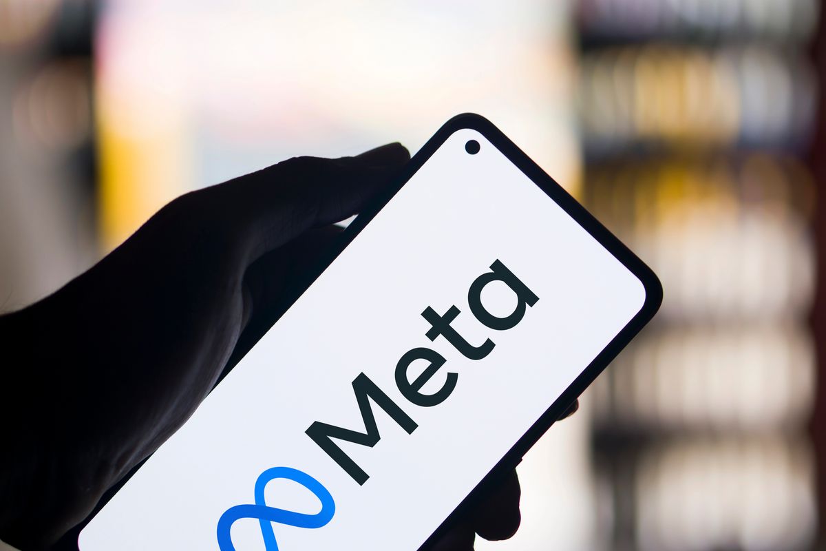 Una mano sostiene un smartphone que muestra el logotipo y el nombre de Meta en su pantalla, con un fondo borroso de luces.