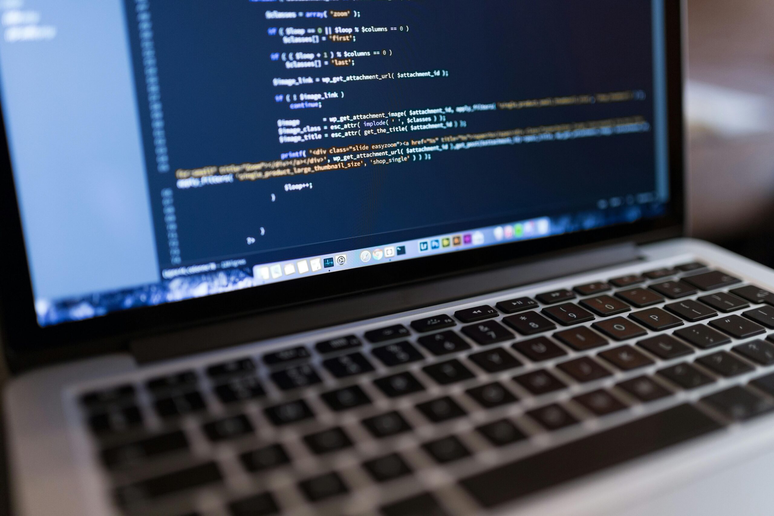 Primer plano de un teclado de ordenador portátil con una pantalla que muestra líneas de código informático en un editor de texto.