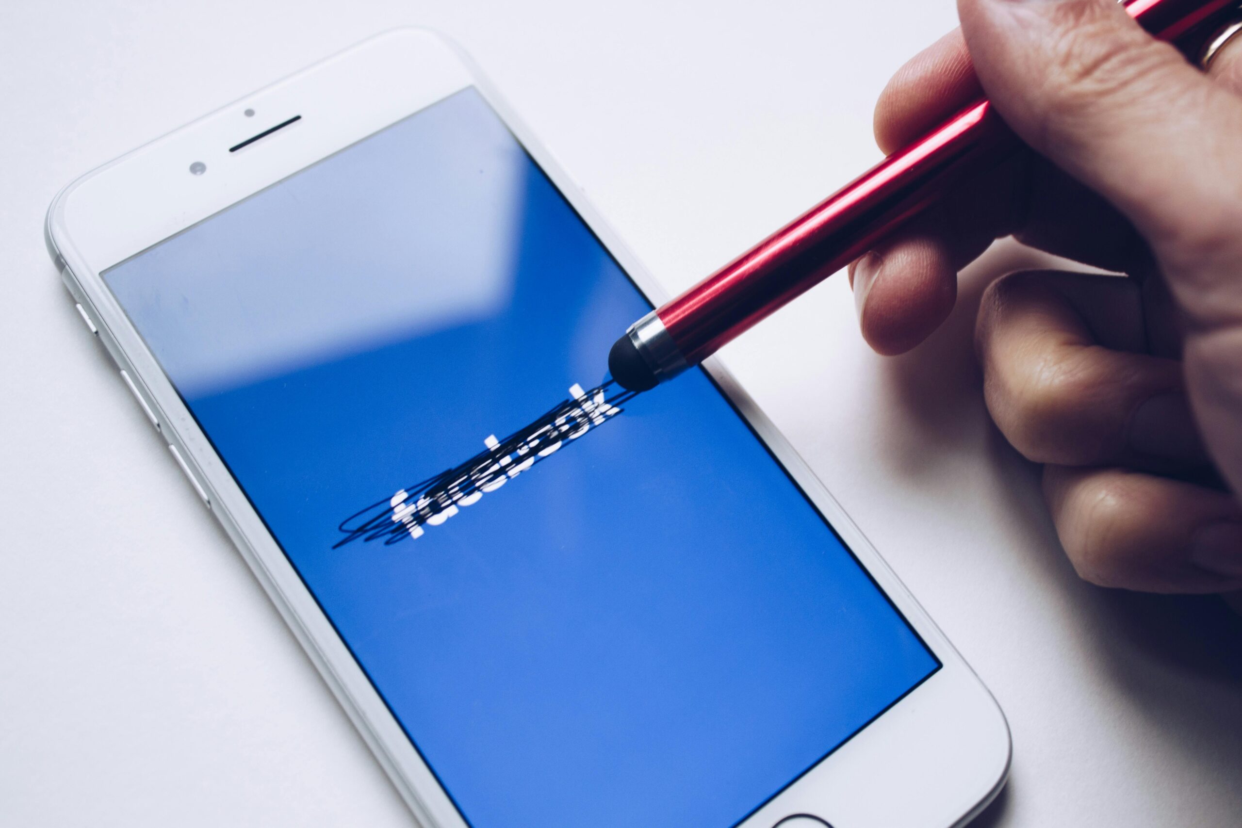 Una mano utiliza un lápiz óptico rojo para tachar el logotipo de Facebook en la pantalla de un smartphone.