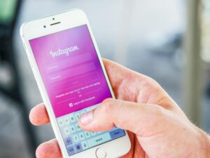 Una persona sostiene un smartphone e inicia sesión en Instagram, con la pantalla rosa de inicio de sesión de la aplicación y un teclado visible para introducir un nombre de usuario y una contraseña.