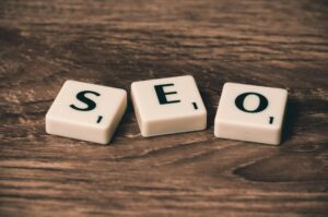 Se colocan tres fichas de Scrabble con la palabra "SEO" sobre una superficie de madera.