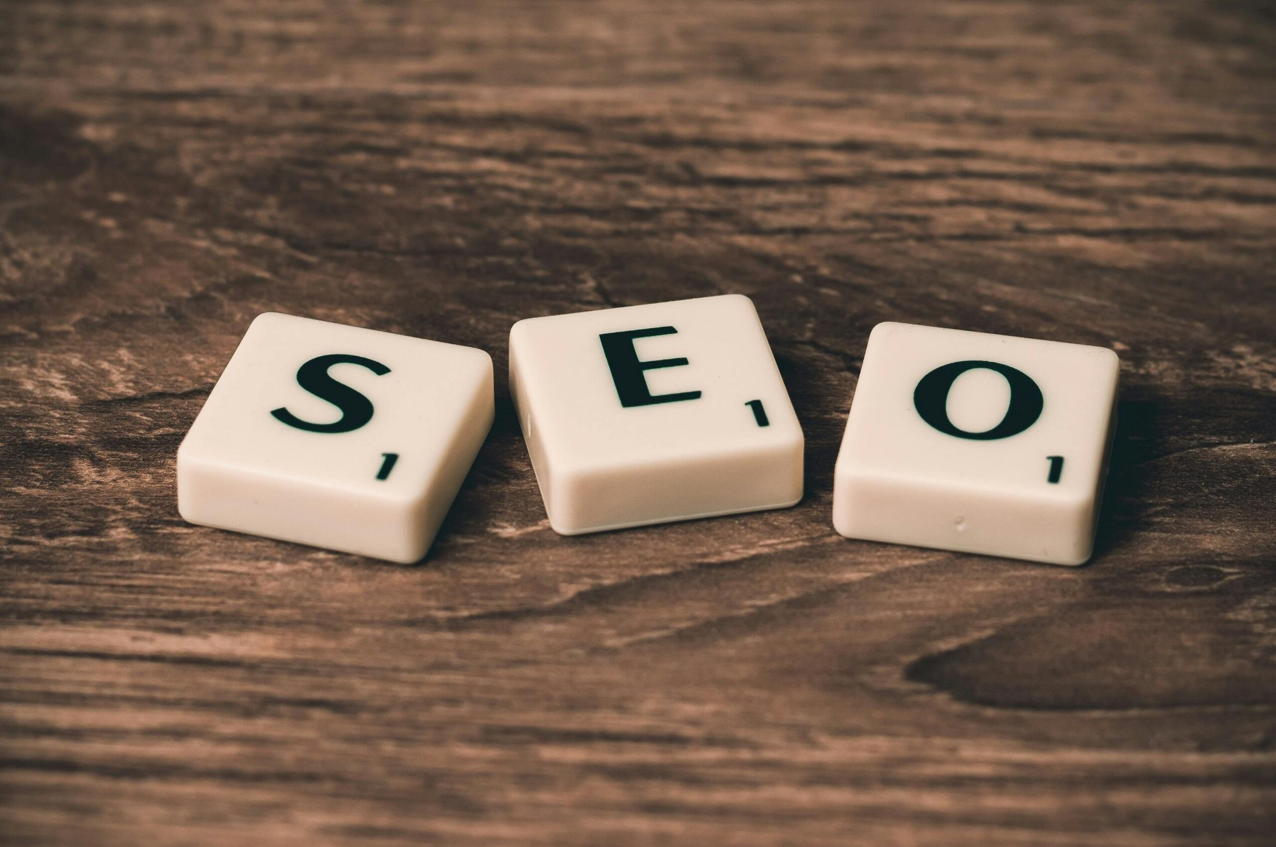 Se colocan tres fichas de Scrabble con la palabra "SEO" sobre una superficie de madera.