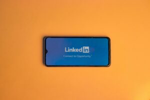 Un smartphone muestra el logotipo de la aplicación LinkedIn y el eslogan "Connect to Opportunity" en una pantalla azul sobre fondo naranja.