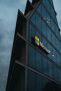 Un moderno edificio de cristal con el logotipo de Microsoft en su exterior, fotografiado desde un ángulo bajo contra un cielo nublado.