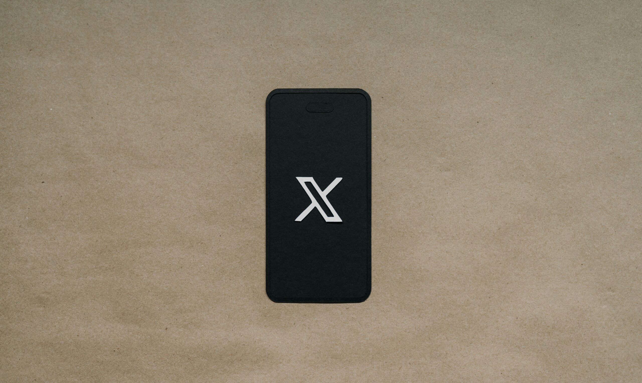 Un smartphone con el logotipo X blanco en la pantalla descansa sobre una superficie lisa de color marrón.