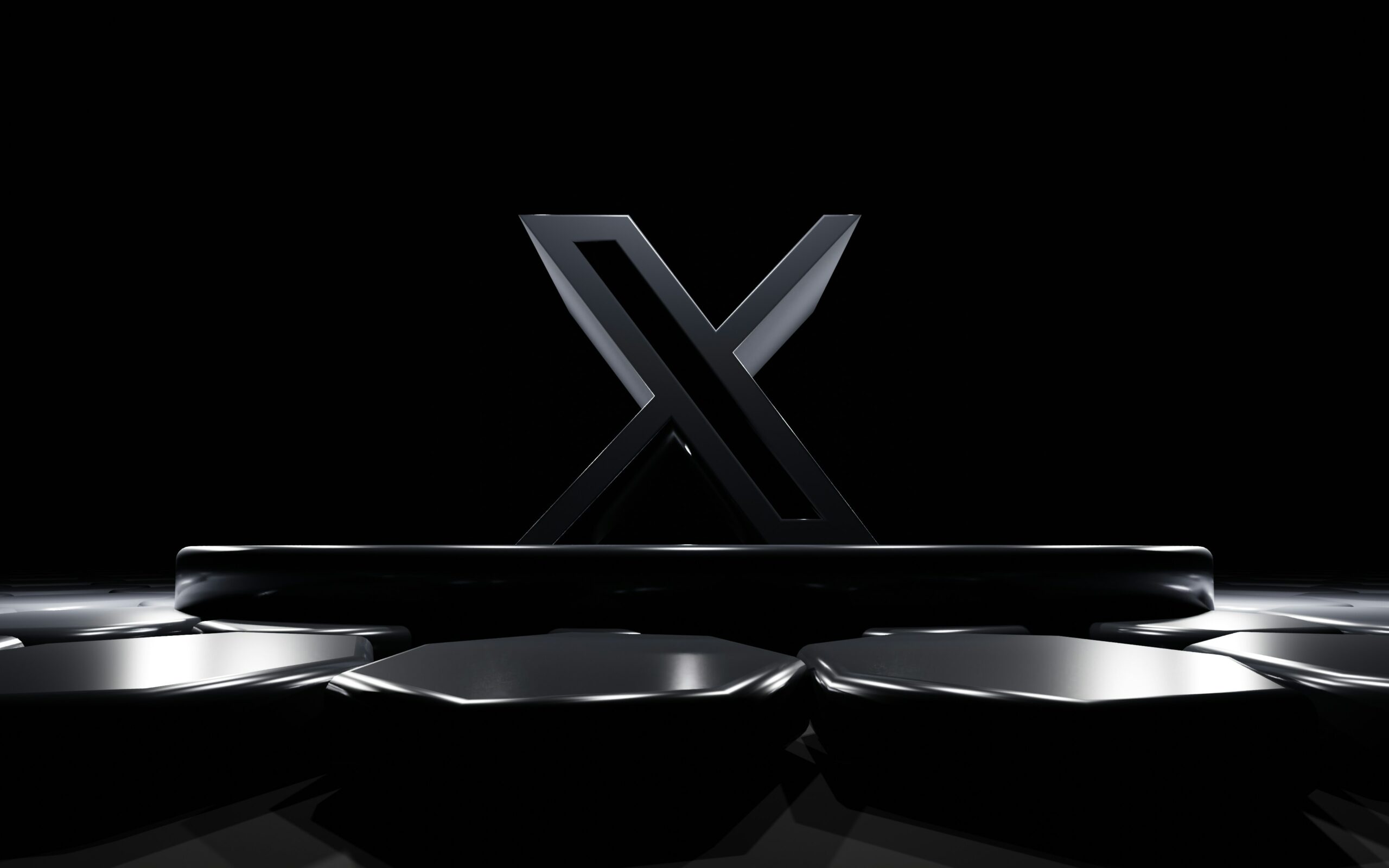 Una escultura en forma de "X" de color negro brillante se alza erguida sobre una plataforma oscura con formas hexagonales en primer plano, sobre un fondo negro.