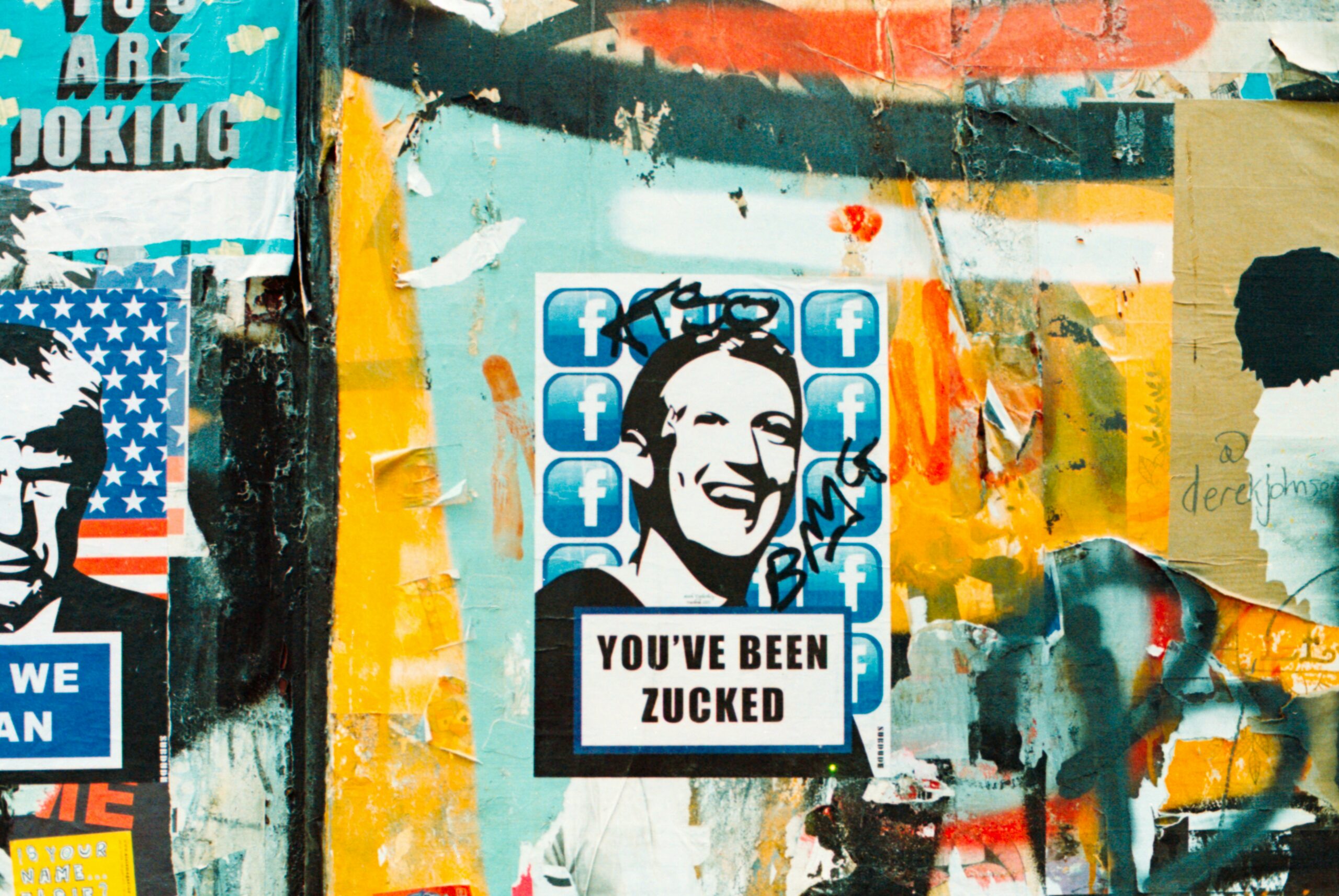 Cartel con el retrato estilizado de un hombre sobre logotipos de Facebook, con la leyenda "YOU'VE BEEN ZUCKED", en una pared cubierta de grafitis de colores y carteles rotos.