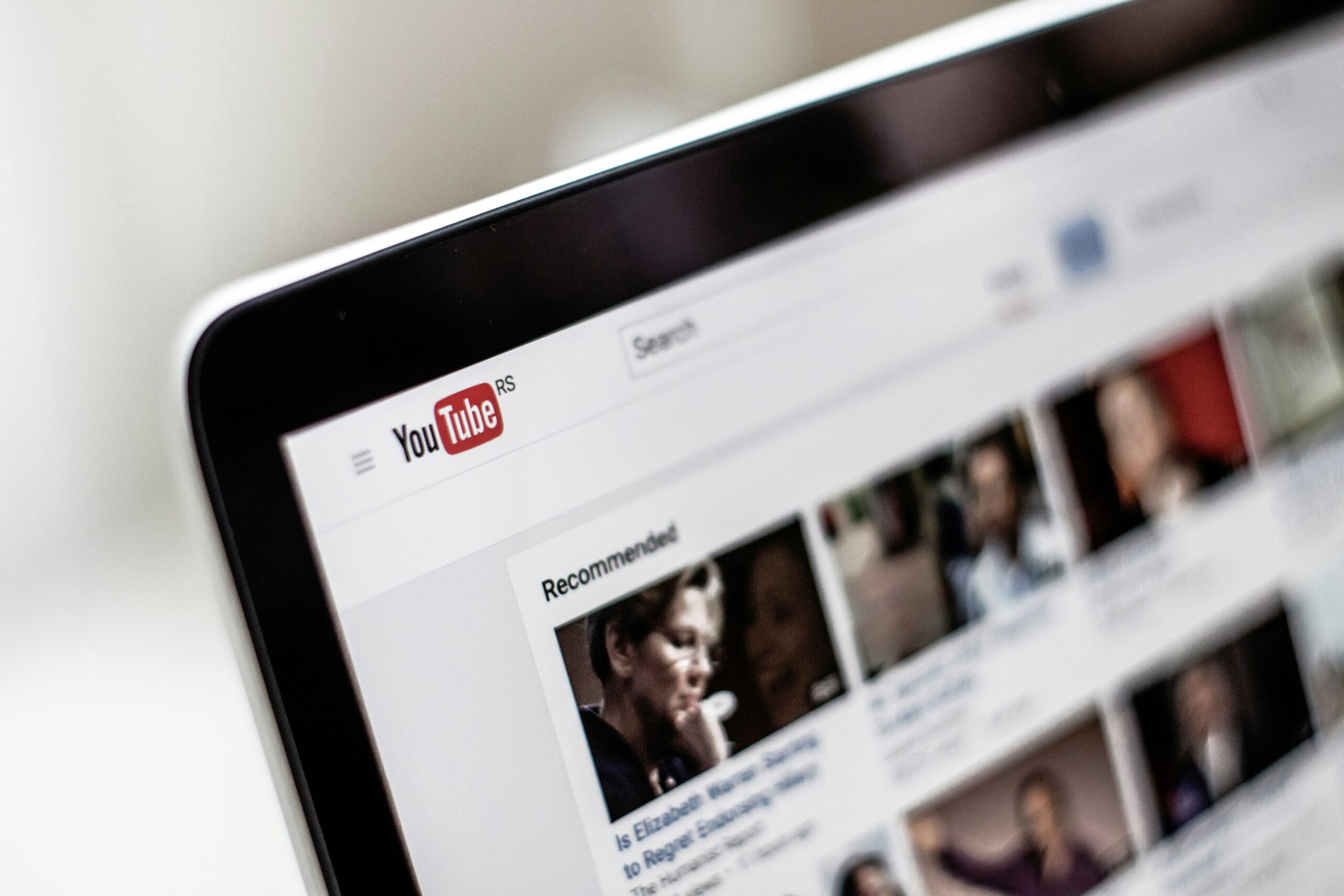 Primer plano de una pantalla de ordenador que muestra la página de inicio del sitio web YouTube con miniaturas de vídeos y la barra de búsqueda visibles.