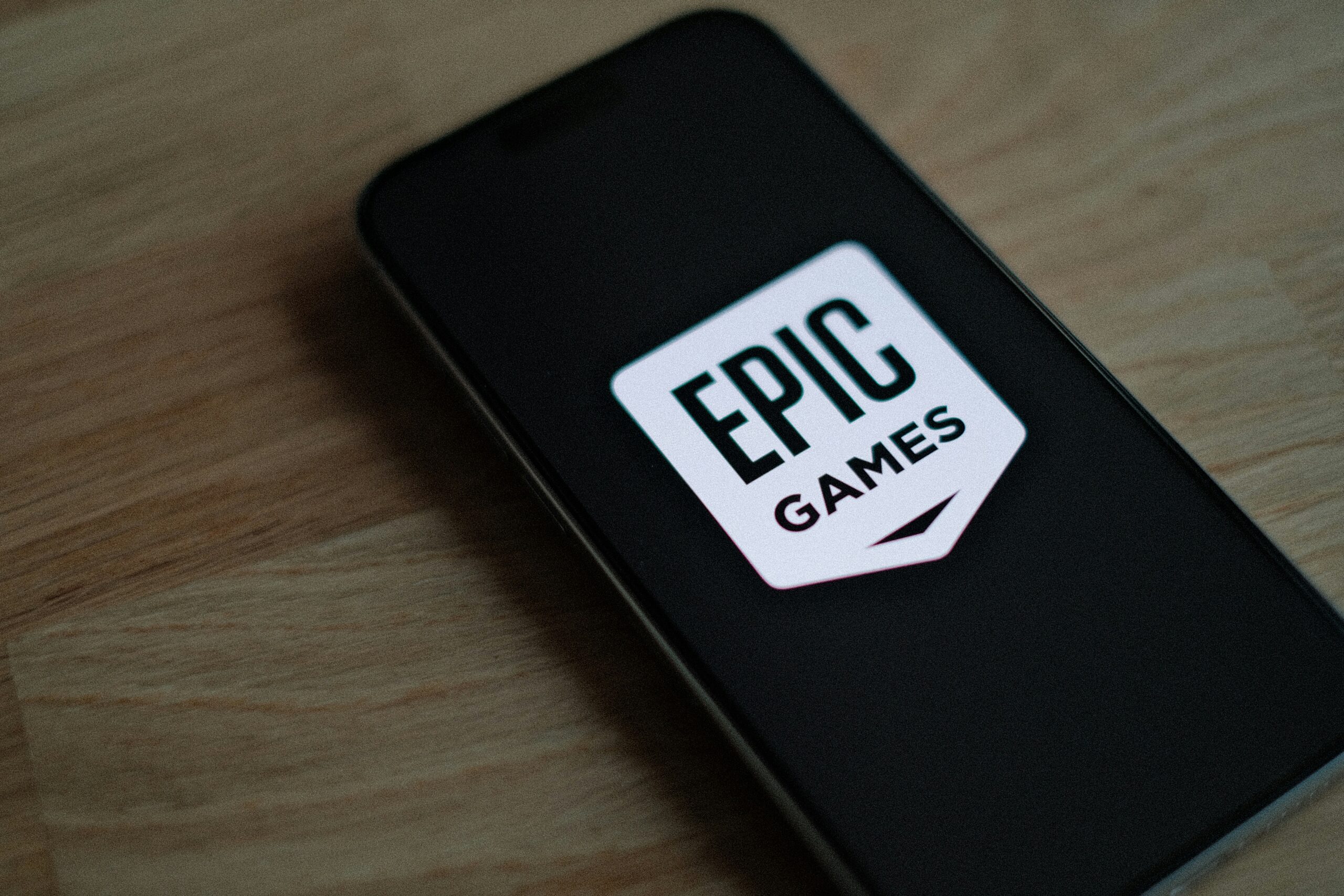 Un smartphone que muestra el logotipo de Epic Games en su pantalla, colocado sobre una superficie de madera.