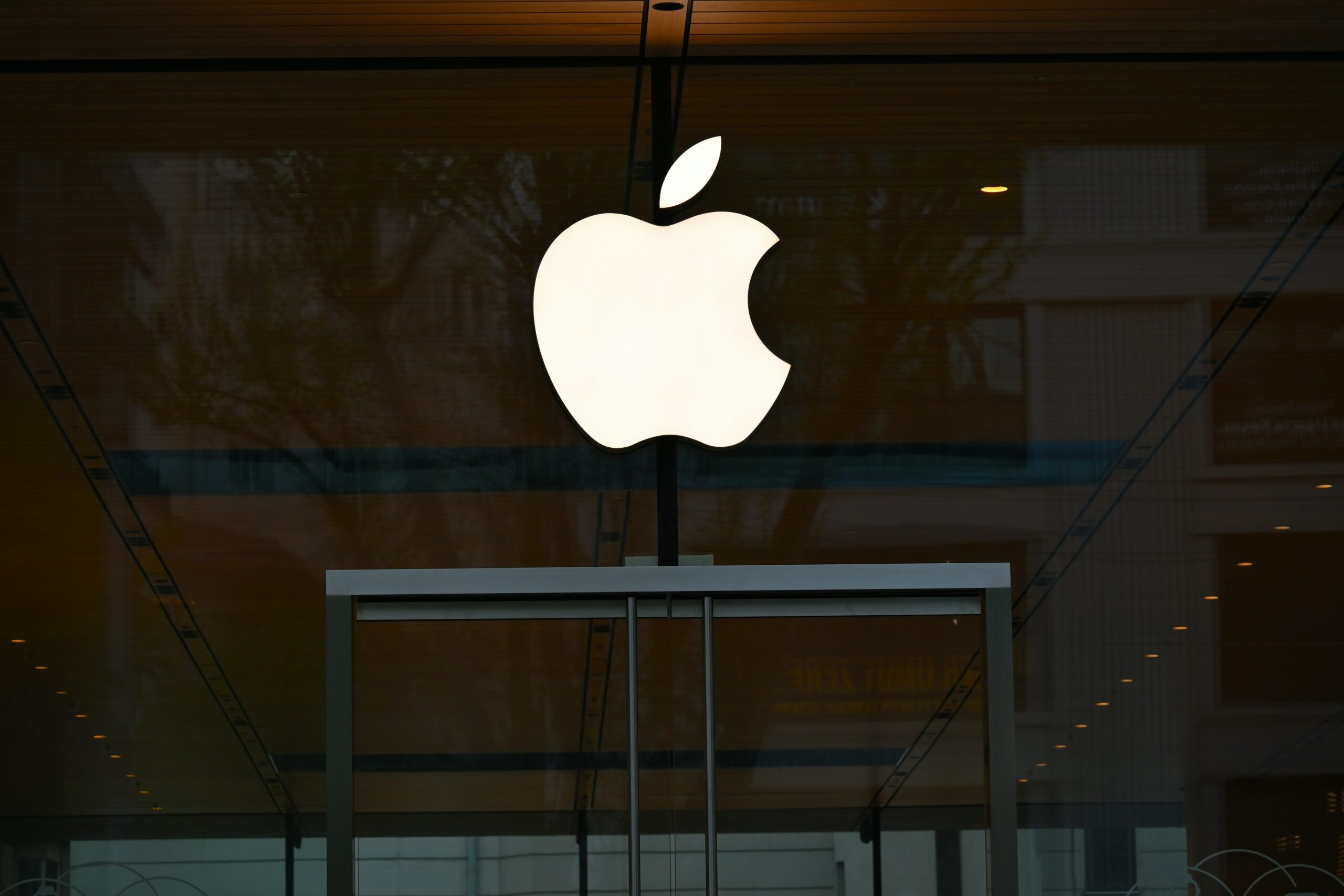 Encima de la entrada de cristal de una tienda Apple aparece un gran logotipo de Apple iluminado en blanco.