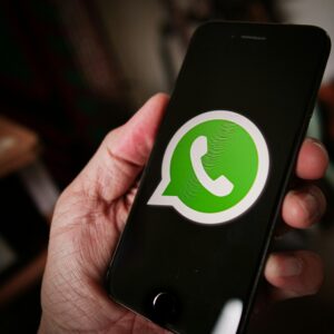 Una persona sostiene un teléfono inteligente en cuya pantalla aparece el logotipo de WhatsApp.