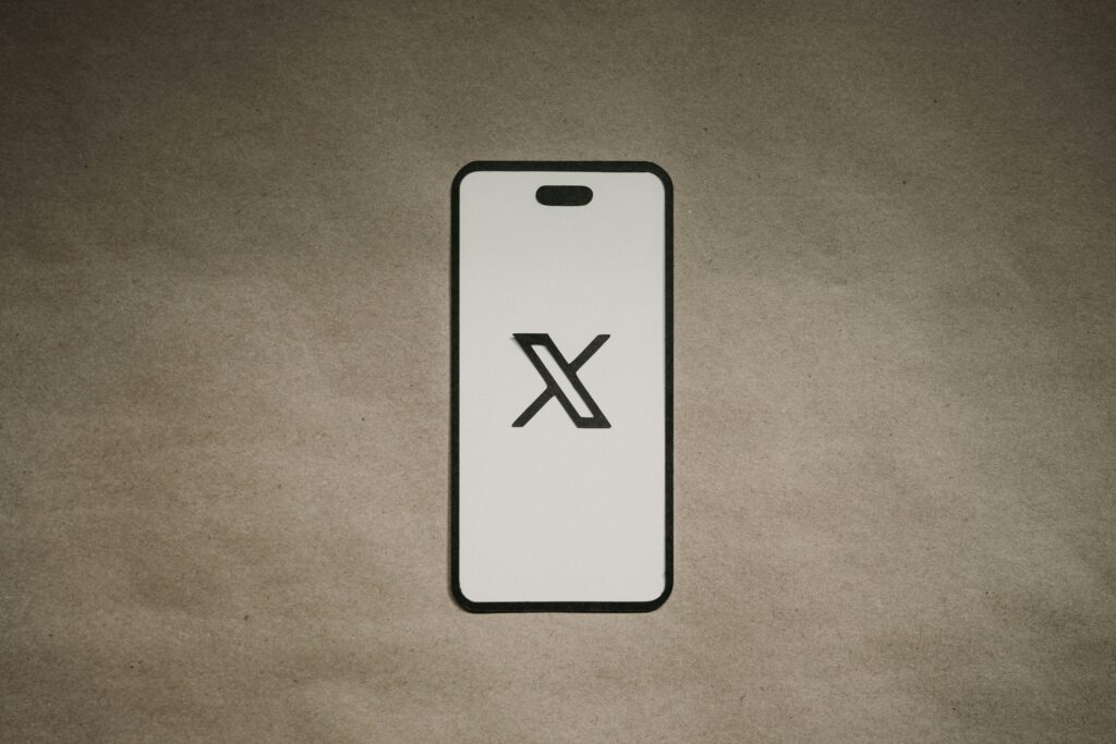 El contorno de un smartphone muestra un gran logotipo "X" negro en su pantalla, centrado sobre un fondo liso marrón texturizado.