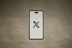 El contorno de un smartphone muestra un gran logotipo "X" negro en su pantalla, centrado sobre un fondo liso marrón texturizado.