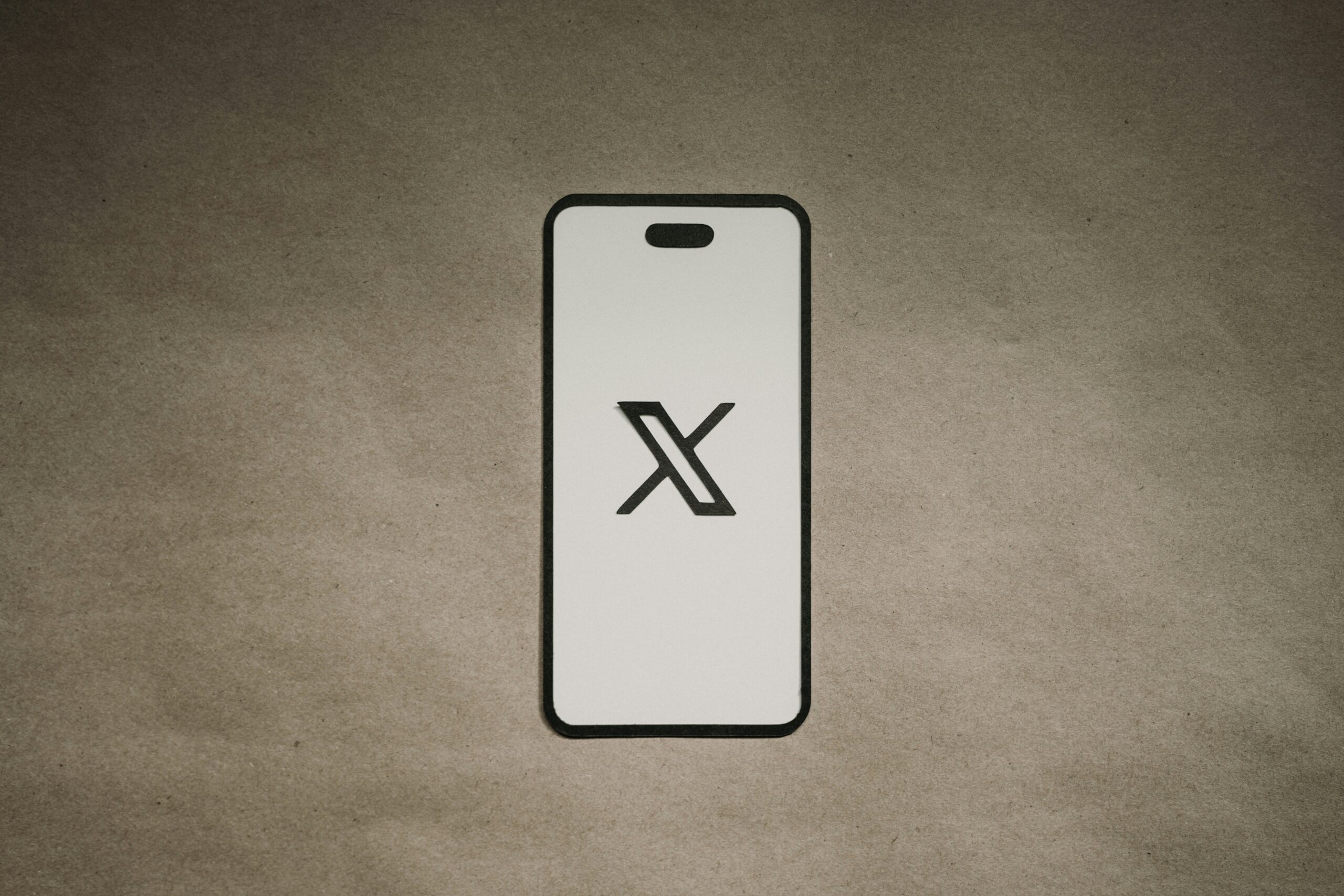 El contorno de un smartphone muestra un gran logotipo "X" negro en su pantalla, centrado sobre un fondo liso marrón texturizado.
