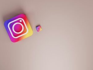 Dos iconos de la aplicación Instagram, uno grande y otro pequeño, se colocan sobre una superficie lisa de color marrón claro con un amplio espacio vacío a la derecha.