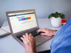Persona escribiendo en un portátil que muestra los análisis de Google Search Console, con una planta y un cuaderno sobre un escritorio blanco.