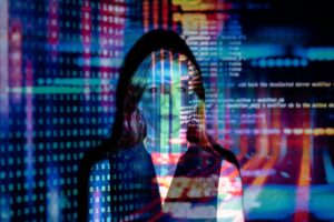 Una mujer de pie frente a una pantalla que muestra líneas de colores de código informático y datos, con las proyecciones superpuestas a su cara y cuerpo.