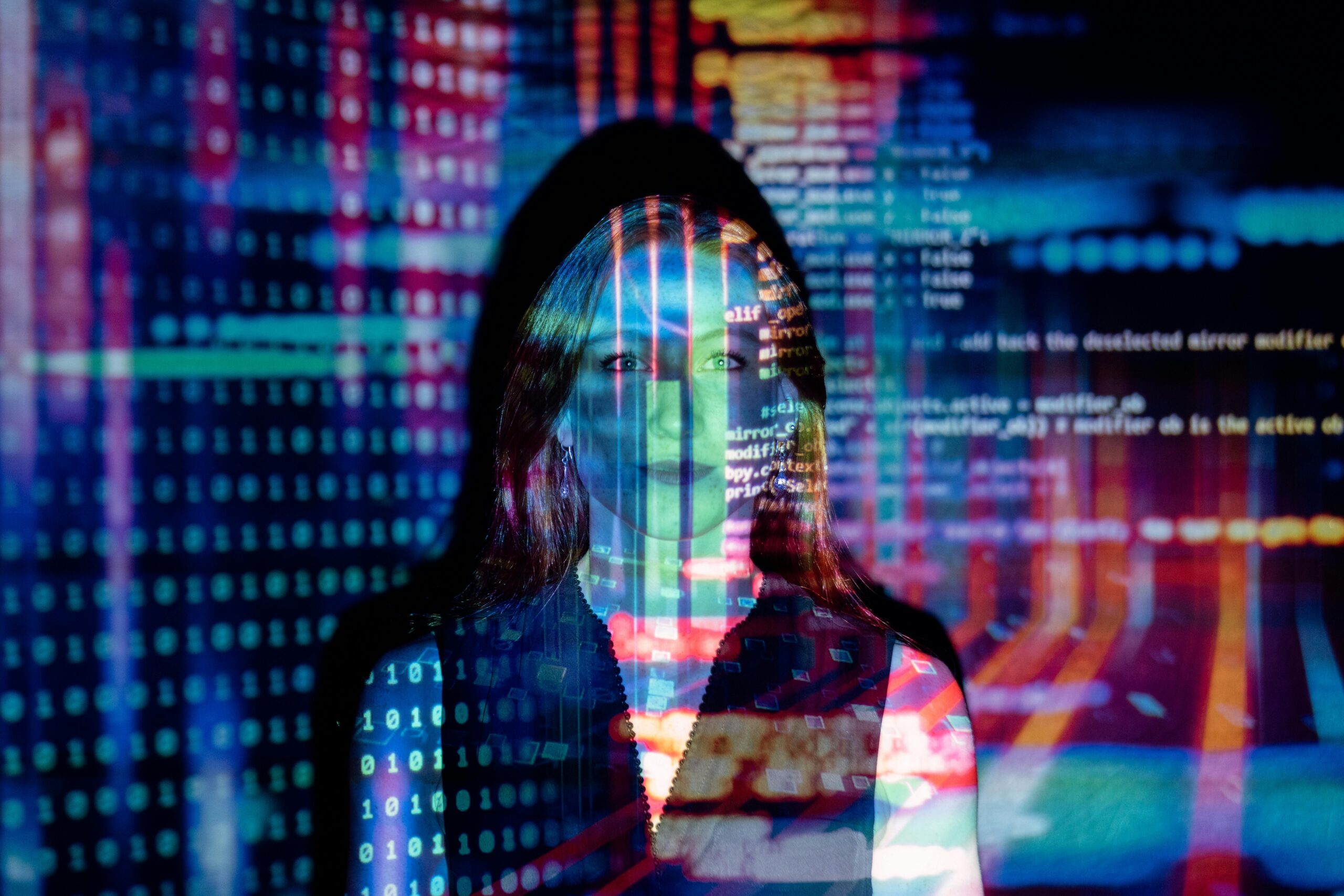 Una mujer de pie frente a una pantalla que muestra líneas de colores de código informático y datos, con las proyecciones superpuestas a su cara y cuerpo.