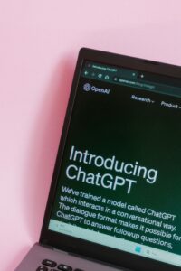 La pantalla de un portátil muestra el sitio web de OpenAI con una página titulada "Introducing ChatGPT" sobre un fondo rosa.