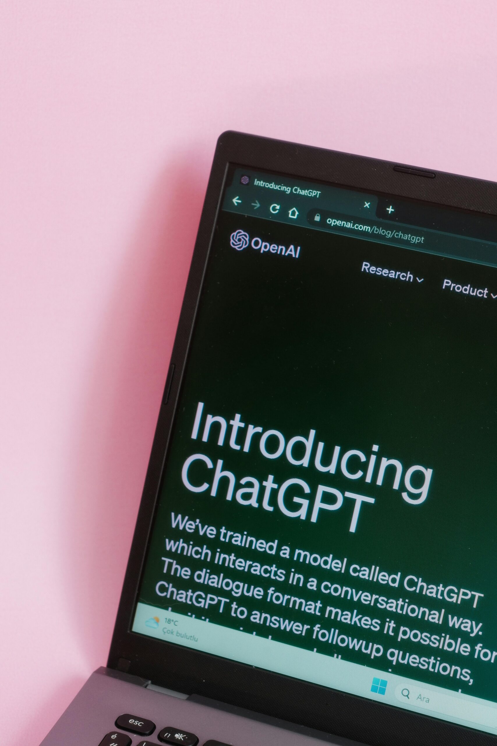 La pantalla de un portátil muestra el sitio web de OpenAI con una página titulada "Introducing ChatGPT" sobre un fondo rosa.