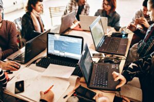 Un grupo de personas trabajando juntas en una mesa con varios ordenadores portátiles, papeles y dibujos técnicos.