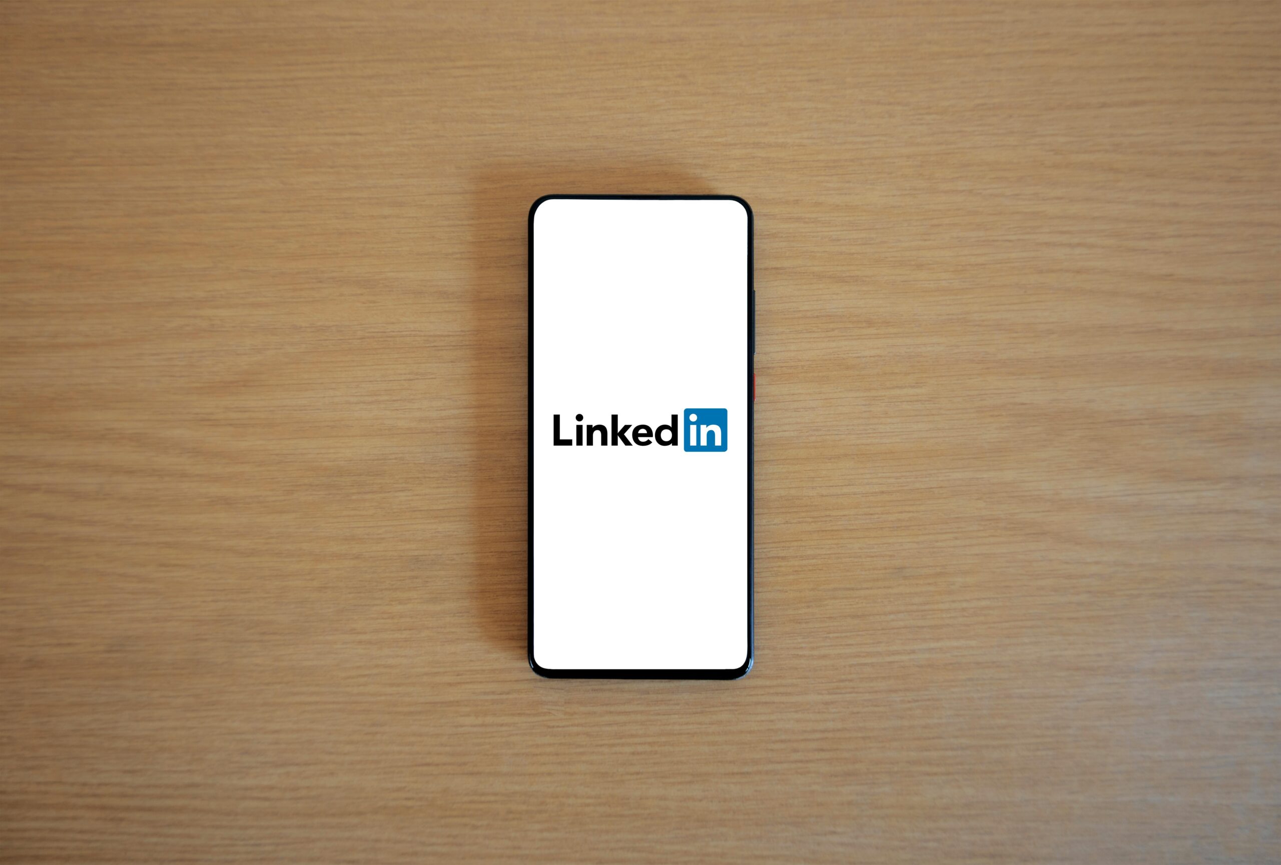 Se coloca un smartphone con el logotipo de LinkedIn en la pantalla sobre una superficie de madera clara.