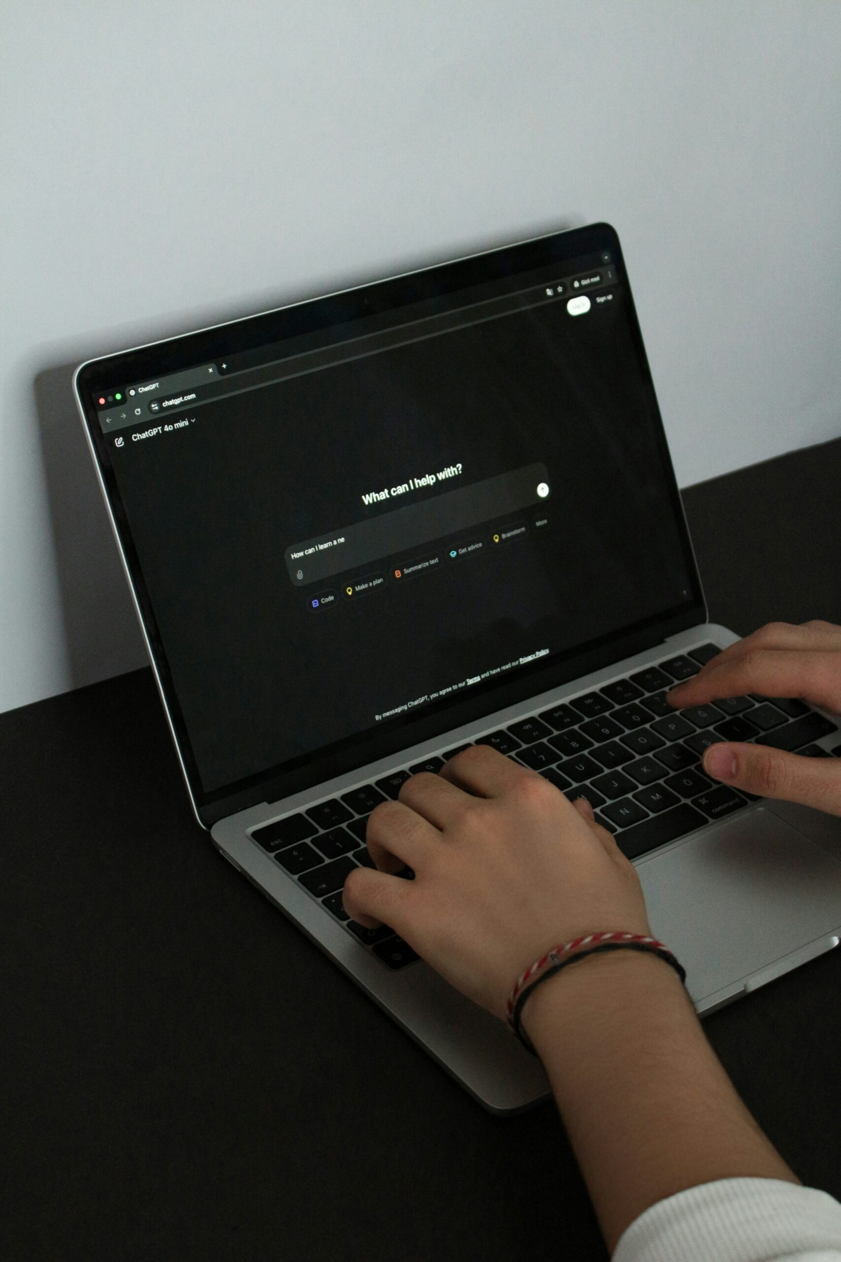 Una persona teclea en un portátil con una pantalla de temática oscura que muestra una interfaz de chatbot que pregunta: "¿En qué puedo ayudarle?.