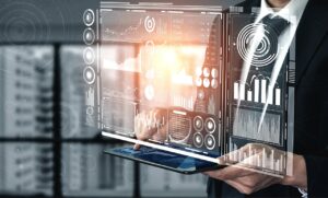 Una persona vestida de traje sostiene una tableta en la que se muestran tablas y gráficos digitales holográficos, que sugieren análisis de datos o analítica empresarial.