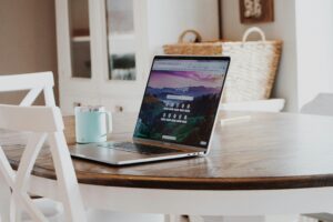 Sobre una mesa redonda de madera y junto a una taza azul claro, en una habitación luminosa y acogedora, hay un ordenador portátil con el navegador abierto.