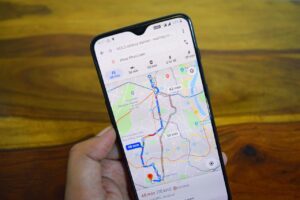 Una mano sostiene un smartphone que muestra una ruta de Google Maps, con indicaciones para llegar desde la estación de tren de NOL hasta el lago Hazur Khwaja.